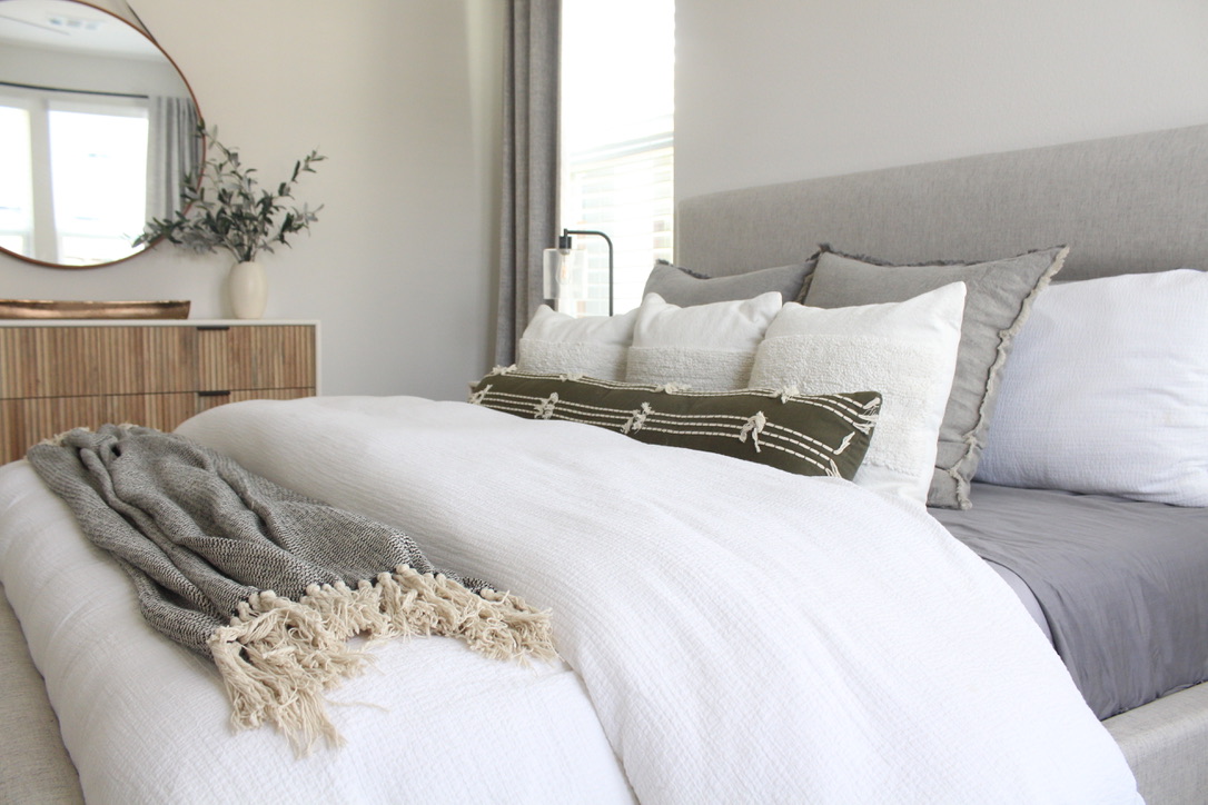 neutral bed with white bedspread and gray pillows in neutral master bedroom